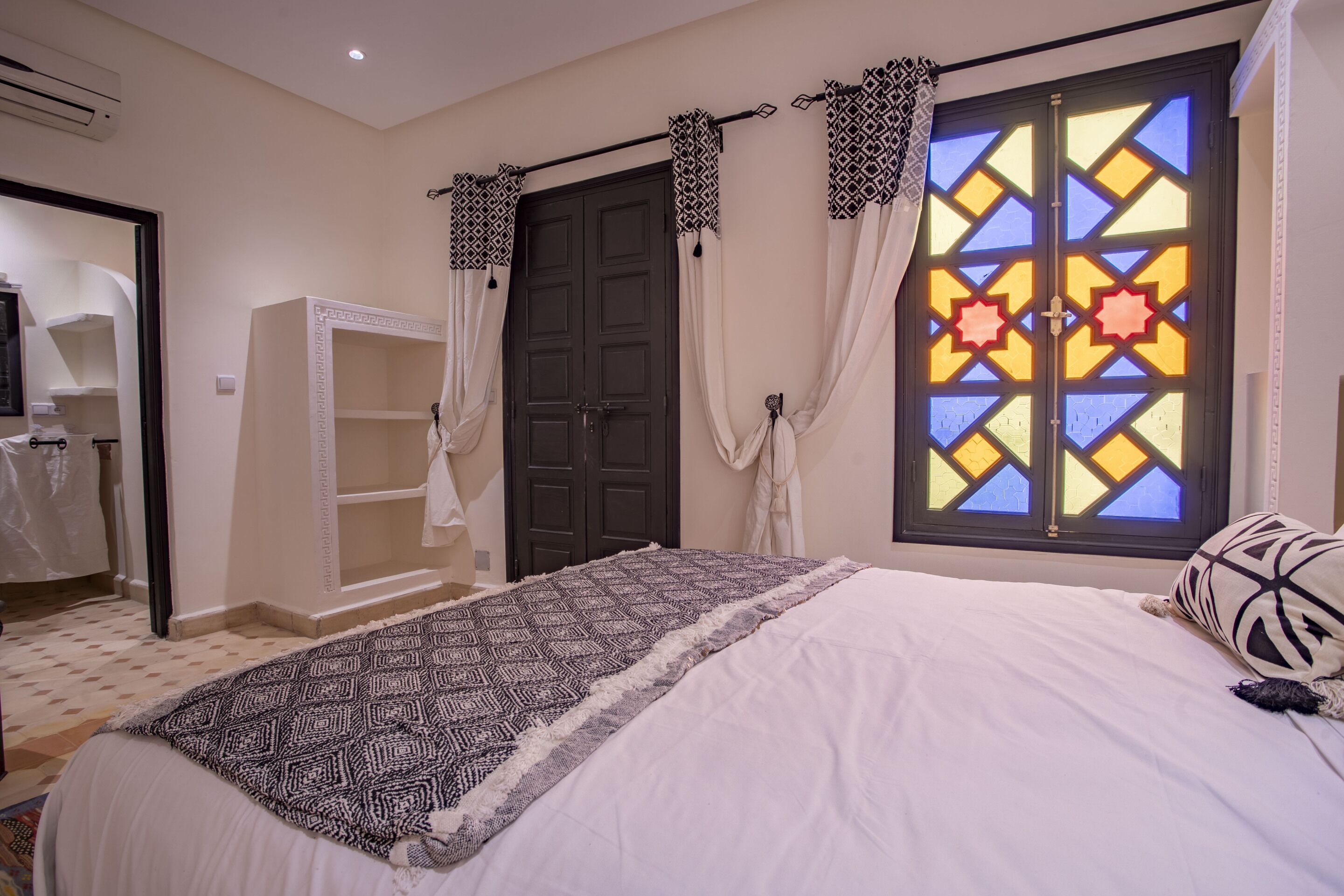 Un dormitorio con cama, armario, ventana con cortinas estampadas y puerta.