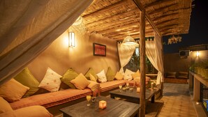 A cozy outdoor seating area with a thatched roof, cushioned sofas, and a wooden coffee table. - Riad tala (Marrakech)