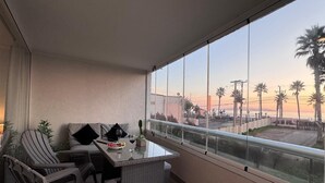 A balcony with a glass railing, a wicker table, and a sofa. - Modern Apartment with Ocean View and Heated Swimming Pool (La Serena)