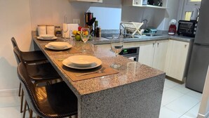 A modern kitchen with granite countertops, a central island with bar stools, and basic appliances. - Modern Apartment with Ocean View and Heated Swimming Pool (La Serena)