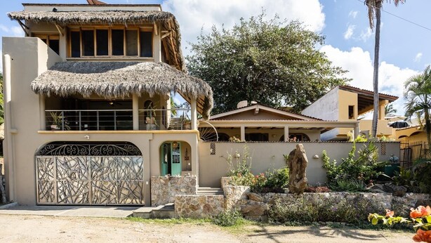 Una casa de dos pisos con techo de paja y una reja metálica decorativa.