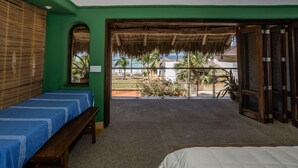 Una habitación con cama, un banco, una ventana con vistas a la playa y una puerta que da al exterior.