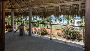 Un espacio al aire libre techado con vista a la playa y palmeras.