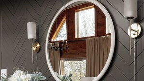 A modern interior with a wooden console table, a round mirror, and a wall-mounted light fixture.