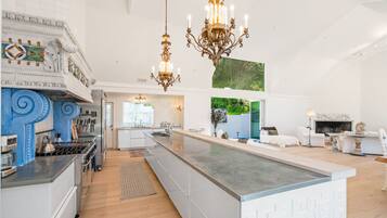 Een ruime keuken met een centraal eiland, een eethoek met witte meubels, en een woonkamer met een open haard.