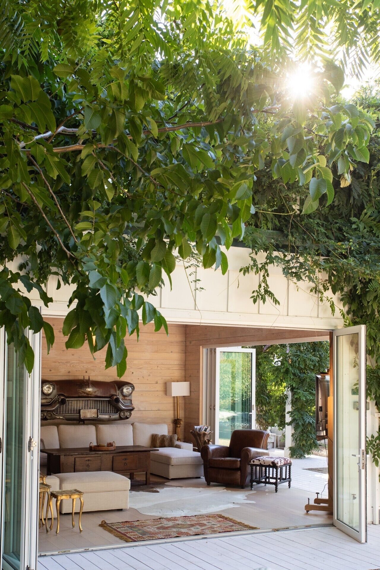 An open-plan living space with a sofa, armchairs, and a coffee table, surrounded by natural light and greenery.