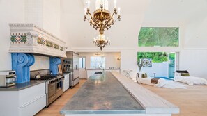 A spacious kitchen with a central island, a dining area, and a large window with a view of greenery.