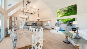 A spacious living area with a large dining table, white chairs, a chandelier, and a view of a lush green landscape. - Kenwood Lodge - 5 Bedroom/En-suite, Heated Pool (Kenwood)