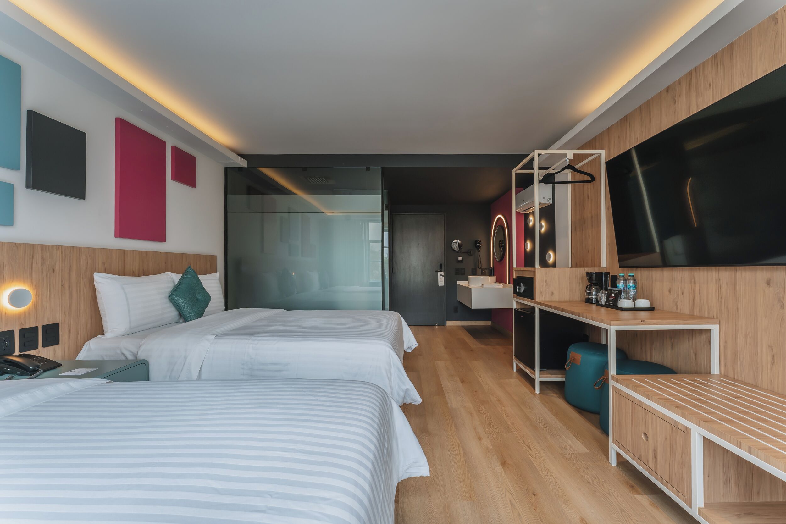 Una habitación de hotel moderna con dos camas, un escritorio, un espejo y un televisor.