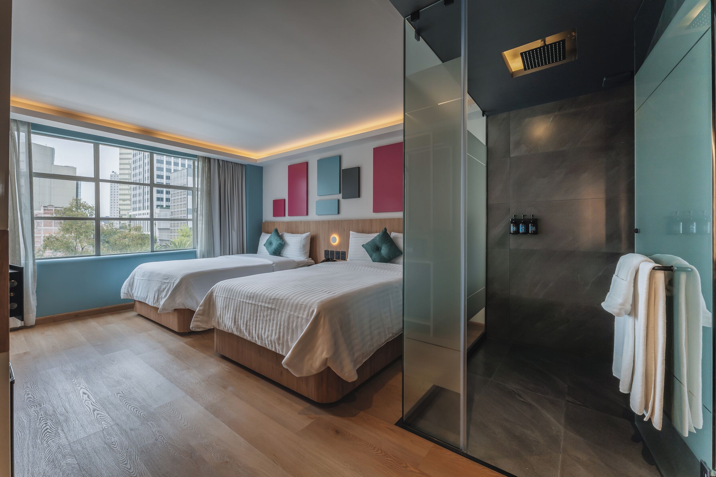 Habitación de hotel moderna con dos camas, cabina de ducha de vidrio y vista a la ciudad.