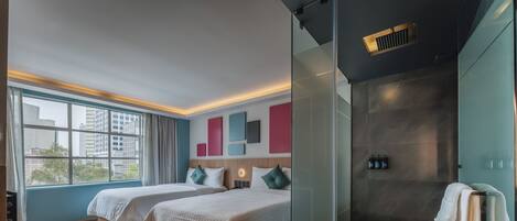 Habitación de hotel moderna con dos camas, cabina de ducha de vidrio y vista a la ciudad.
