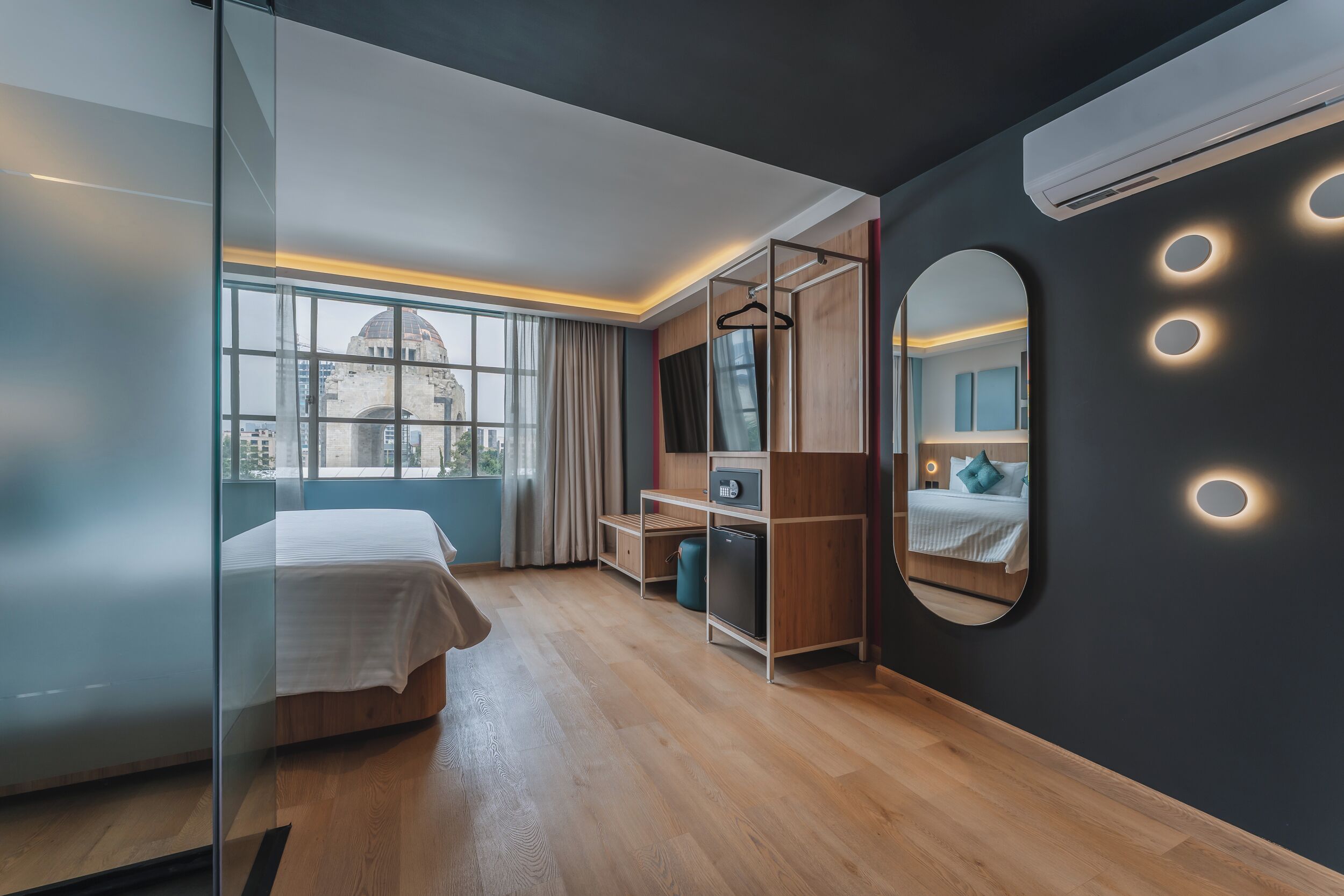 A modern hotel room with a bed, a desk, a wardrobe, and a large mirror.