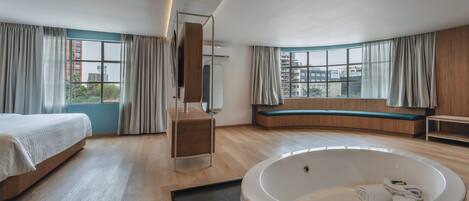 Une chambre d’hôtel moderne dotée d’une grande baignoire, d’un lit, d’un coin salon et offrant une vue sur la ville.