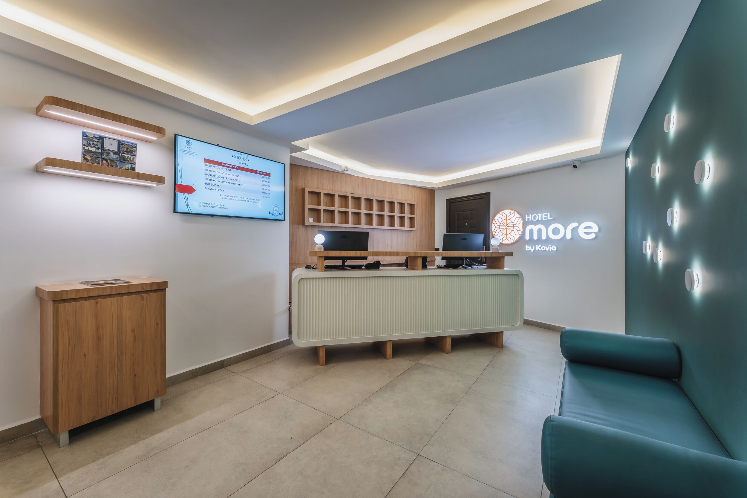 Una moderna zona de recepción con una pantalla digital, mostrador de madera y un área de asientos color turquesa.