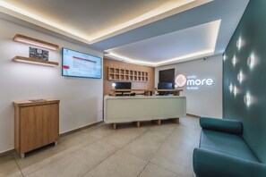 A modern reception area with a digital display, wooden reception desk, and a teal seating area. - HOTEL MORE BY KAVIA (Mexico City)