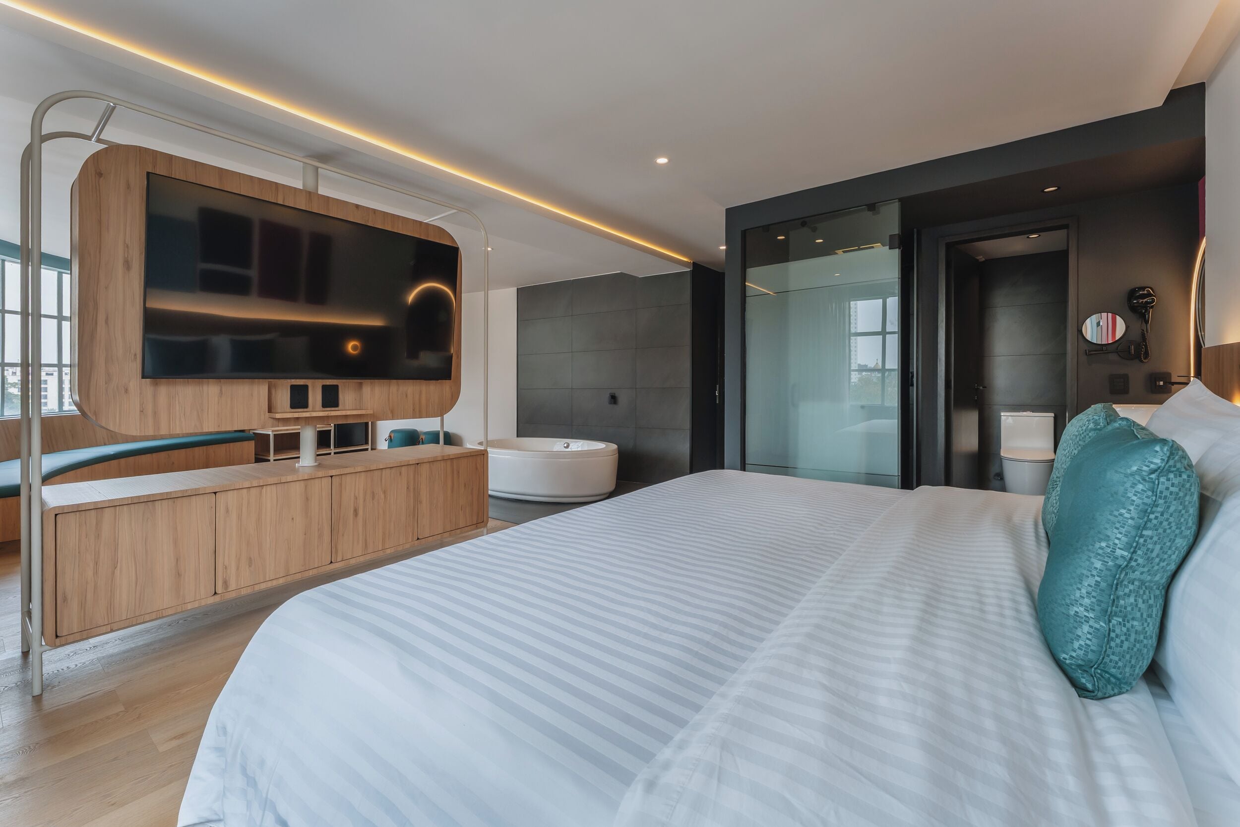 Habitación de hotel moderna con una cama grande, televisión integrada, bañera y zona de ducha con paredes de vidrio.