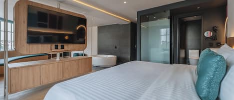 Habitación de hotel moderna con una cama grande, televisión integrada, bañera y zona de ducha con paredes de vidrio.
