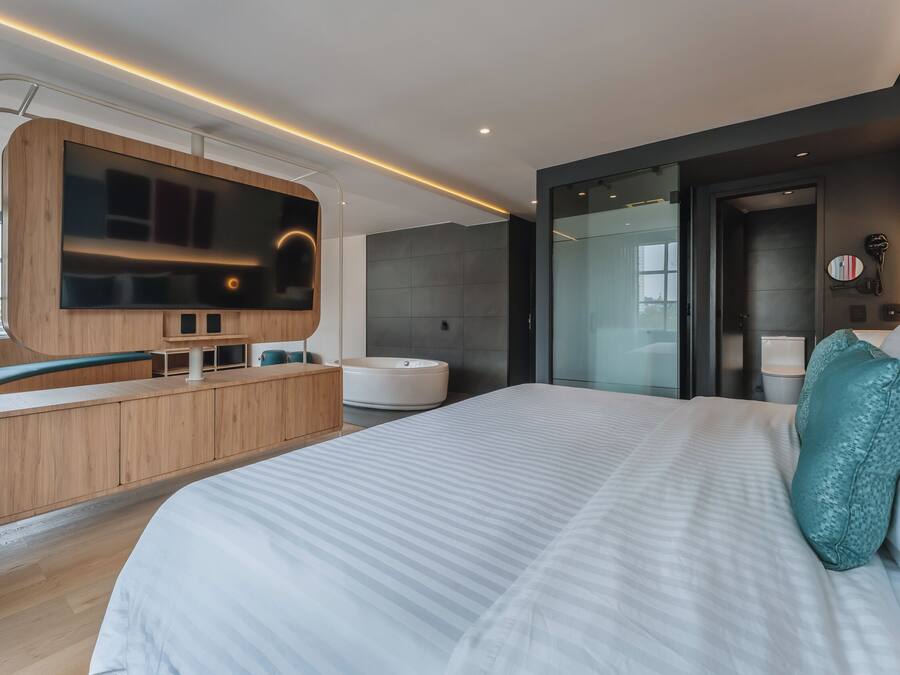 Habitación de hotel moderna con una cama grande, televisión integrada, bañera y zona de ducha con paredes de vidrio.