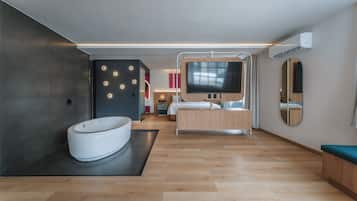 Una habitación de hotel moderna con una bañera grande, una cama, un televisor y un espejo.