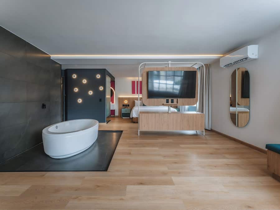 Une chambre d’hôtel moderne équipée d’une grande baignoire, d’un lit, d’une télévision et d’un miroir.