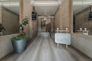 Un moderno vestíbulo de hotel con una recepción, una planta grande en maceta y una escalera que lleva a los pisos superiores.