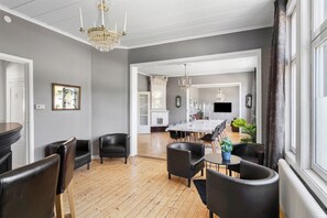Un comedor espacioso con una larga mesa y numerosas sillas, un candelabro, y vistas a una cocina y zona de estar a través de un arco abierto.