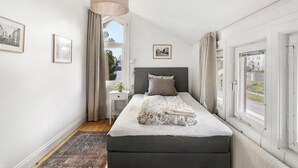 Un dormitorio con cama, mesita de noche, lámpara y ventana con cortinas.