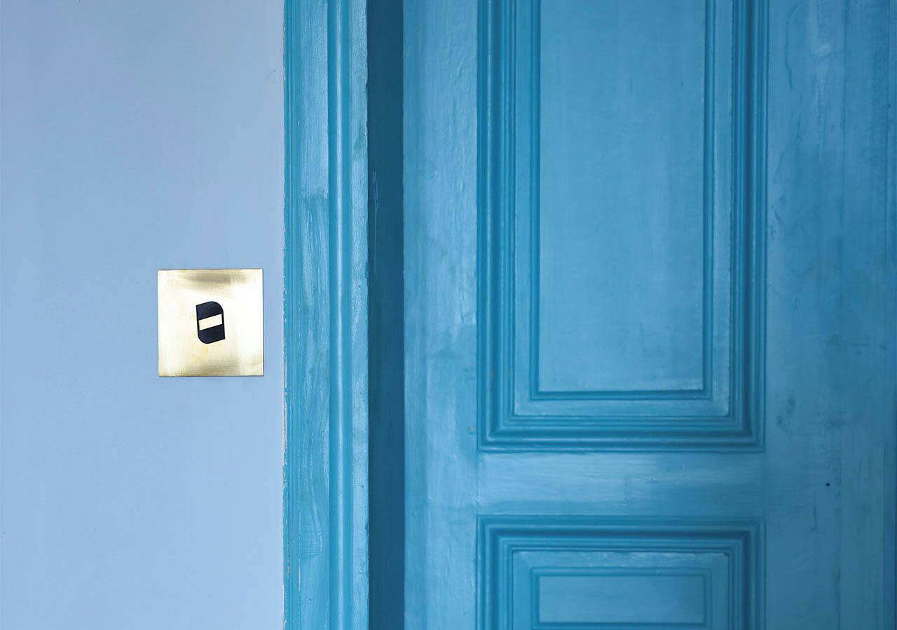 Une porte bleue avec un cadenas en laiton et une plaque métallique carrée dotée d’un trou de serrure.