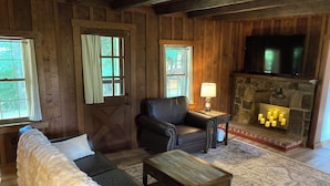 A cozy cabin interior with a fireplace, leather sofa, and a television. - Tarry Moore Cottage ... on Foxburg's historic fairways (Foxburg)
