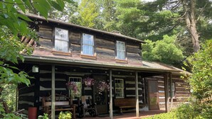 A rustic log cabin with a porch, potted plants, and a bench. - Tarry Moore Cottage ... on Foxburg's historic fairways (Foxburg)