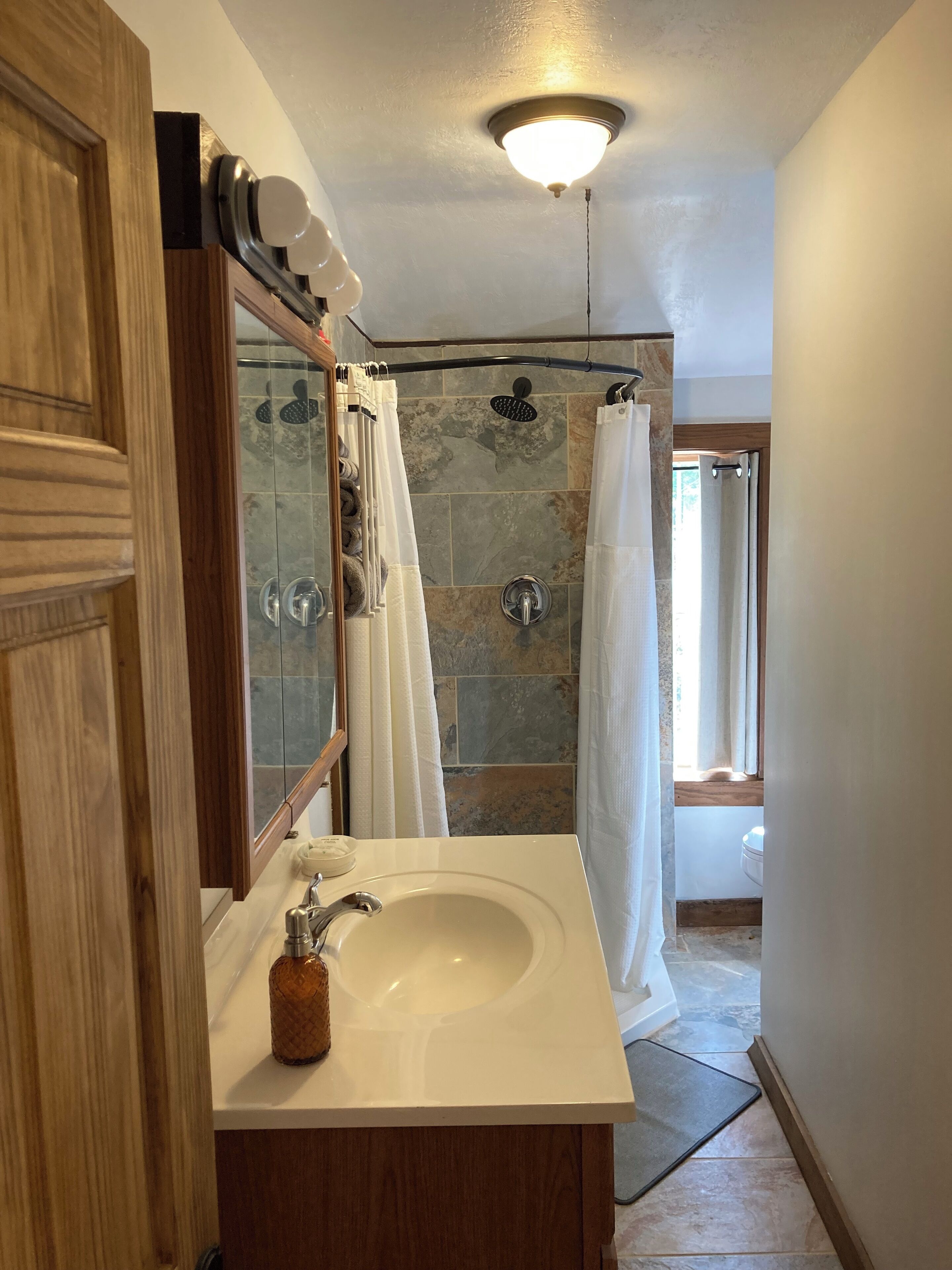 A bathroom with a white sink, a mirror, a shower with a glass door, and a ceiling light.