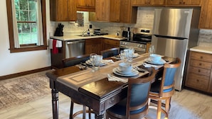A modern kitchen with wooden cabinets, a stainless steel refrigerator, and a dining area set for four. - Tarry Moore Cottage ... on Foxburg's historic fairways (Foxburg)