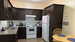 A kitchen with dark wooden cabinets, a white stove, and a white refrigerator. There is a wooden table with two blue placemats. - Kate's Cove in North Nanaimo - quiet location, 5 minute walk to ocean (Nanaimo)