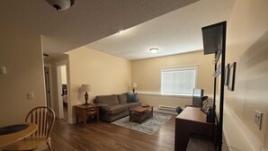A living room with a sofa, coffee table, TV, and a dining area with a table and chairs. - Kate's Cove in North Nanaimo - quiet location, 5 minute walk to ocean (Nanaimo)