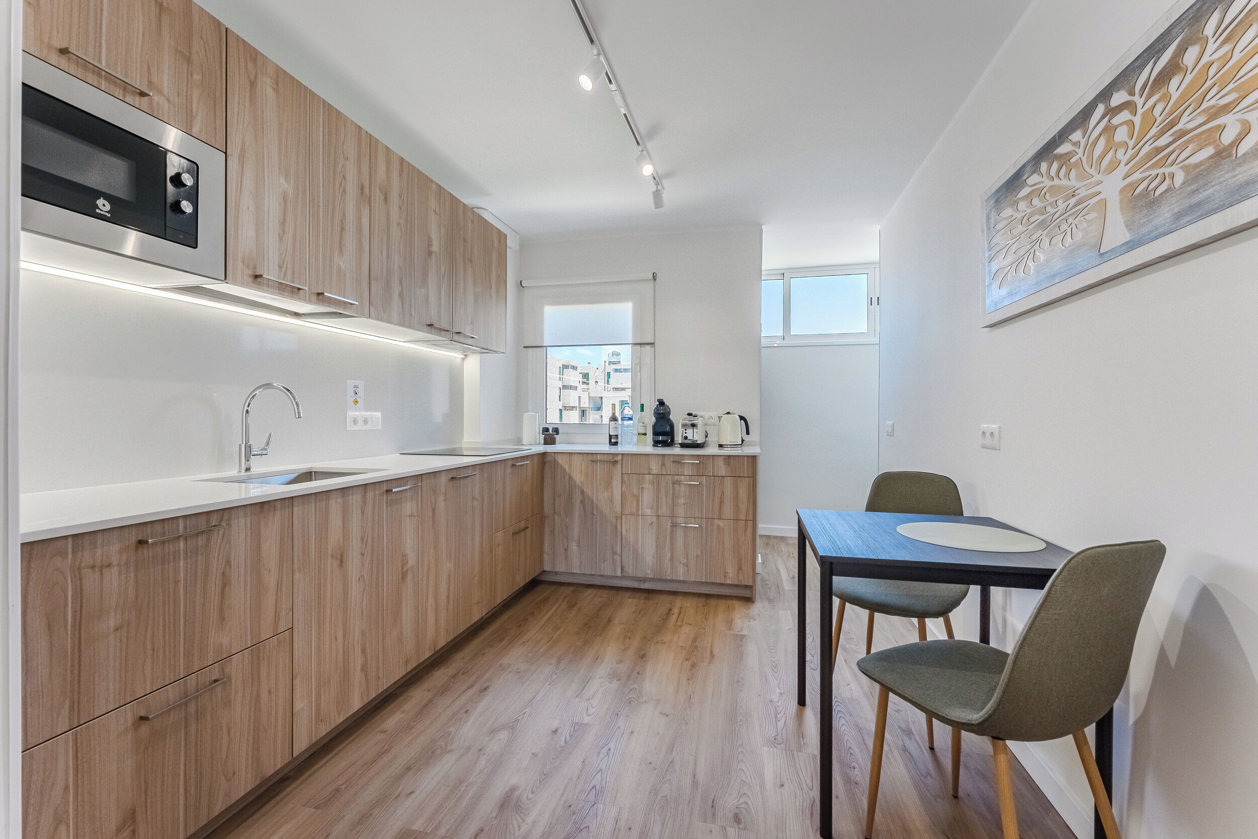 Eine moderne Küche mit Holzschränken, einer eingebauten Mikrowelle und einem Essbereich mit Tisch und Stühlen.