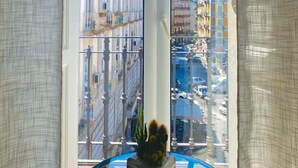 A room with a large window offering a view of a city street with buildings and parked cars. - Nerisa home  (Naples)