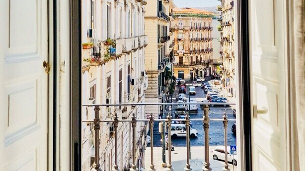 A view from an open door of a building with a street in front, featuring multiple buildings and parked cars. - Nerisa home  (Naples)