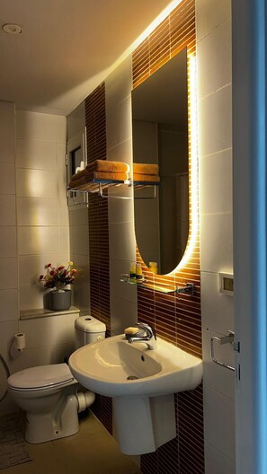 Ein modernes Badezimmer mit Waschbecken, Toilette, Spiegel mit LED-Beleuchtung und Handtuchhalter.