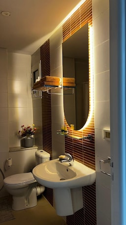 A modern bathroom with a toilet, sink, and a mirror with built-in lighting.. Your elegant and spacious Chez-Moi retreat in the heart of Sfax