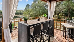 Une terrasse extérieure aménagée avec des meubles en osier, une table en bois et une vue sur une rivière et des arbres.