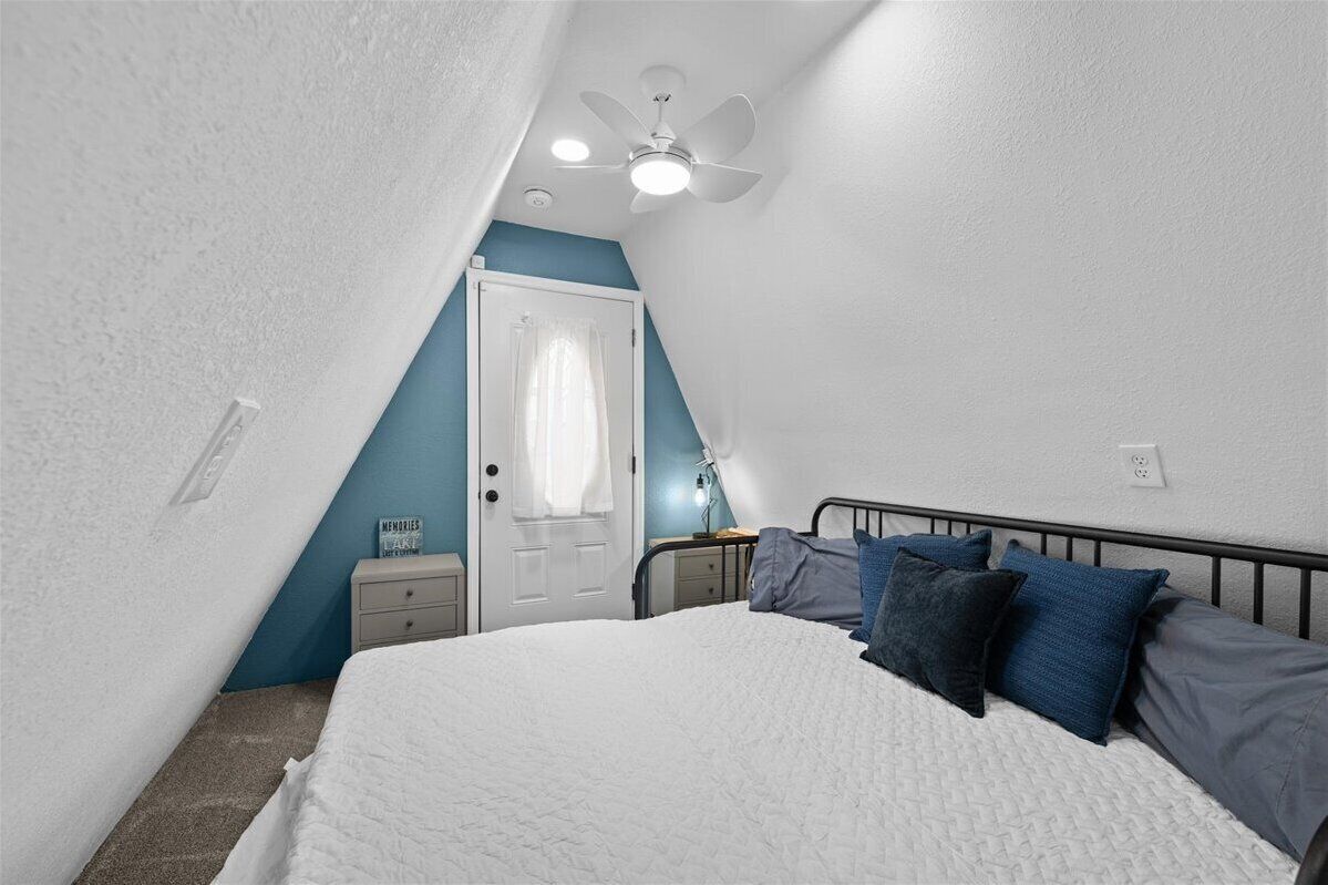 Une chambre à coucher comprenant un lit, une table de chevet, une lampe, un ventilateur de plafond et une porte.