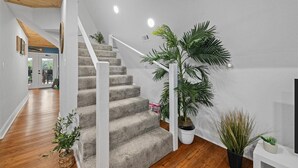 Un escalier dont les marches sont recouvertes de moquette, avec des rampes blanches et des plantes en pot.