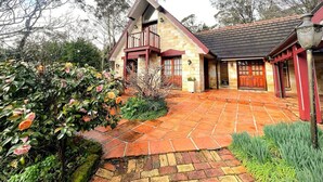A two-story stone house with a balcony, a stone-paved driveway, and surrounding greenery. - Gingerbread House – sunset, relaxing & warm (Katoomba)