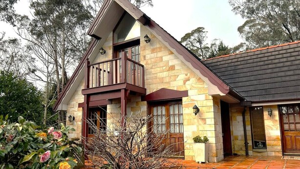 A two-story stone house with a balcony, a tiled driveway, and a garden with flowering plants. - Gingerbread House – sunset, relaxing & warm (Katoomba)