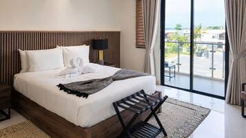 Quarto de hotel com uma cama grande, cabeceira de madeira, mesa de cabeceira com abajur e vista para o exterior através de uma janela ampla.
