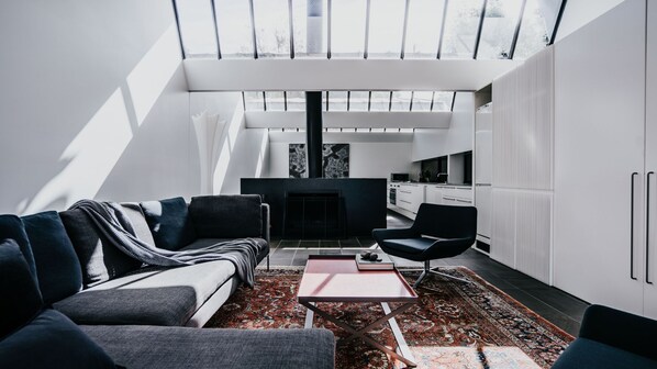 Un salon moderne avec un canapé, une table basse et une cheminée. Il y a également un coin cuisine avec des meubles blancs et une table à manger.