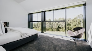 Un dormitorio con un ventanal grande, una cama, una silla y vistas a árboles.