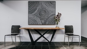 A reception desk with a wooden top and black metal legs, flanked by two black wicker chairs. A large black and white abstract artwork hangs above the desk.