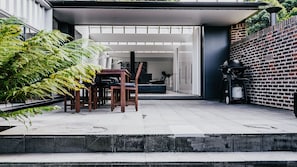 Une terrasse extérieure avec une table et des chaises, un mur en briques et un réchaud à gaz.