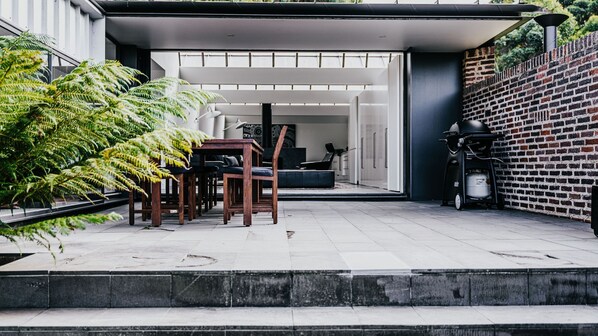 An outdoor patio with a dining table and chairs, a brick wall, and a gas stove.